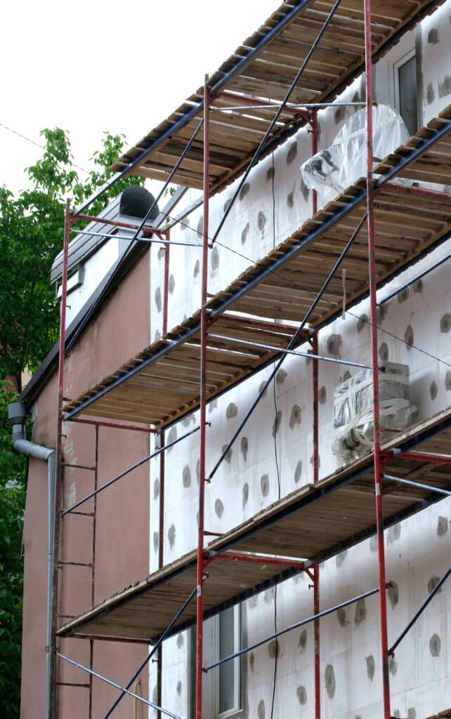 Échafaudage et isolation de façade pour rénovation de maison Façade en rénovation avec échafaudage. Panneaux d'isolation en polystyrène fixés au mur par des plots de mortier. Matériaux de construction.