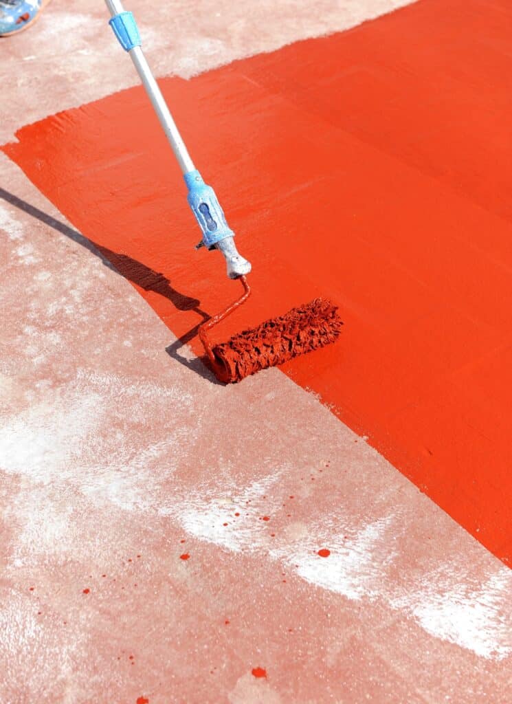 Peinture rouge intense : application au rouleau sur sol Application de peinture rouge intense au rouleau sur un sol en béton. La surface est divisée entre la couleur vibrante et le béton brut.