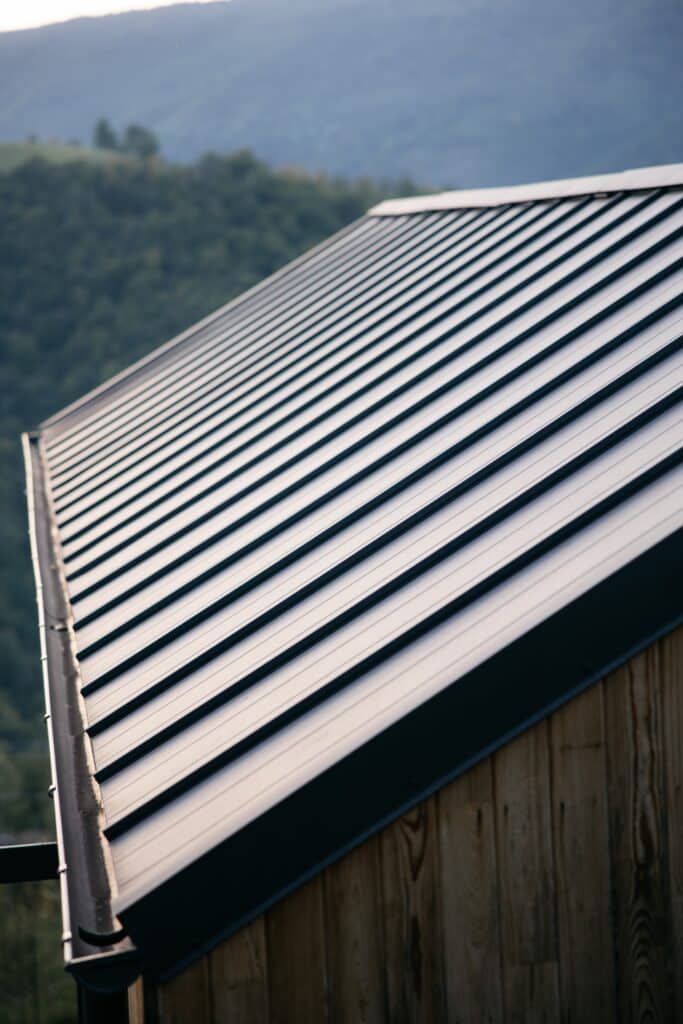 Toit métallique joint debout : design moderne en montagne. Toit métallique gris à joint debout sur bardage bois rustique, avec gouttière, contre fond de montagnes verdoyantes floues.